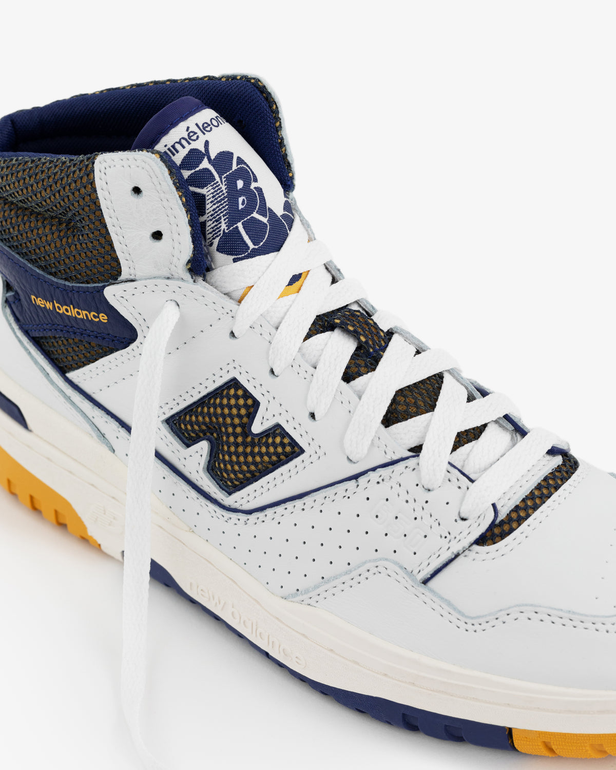 A close-up of the ALD / New Balance 650R in white with blue and gold accents and a partially untied lace.