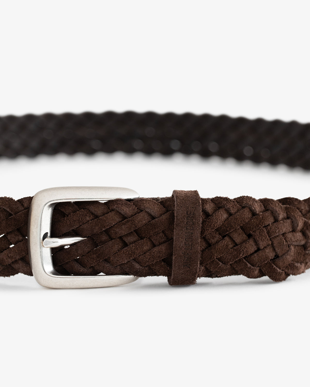Close-up of a Braided Suede Belt in brown with a silver buckle on a white background.