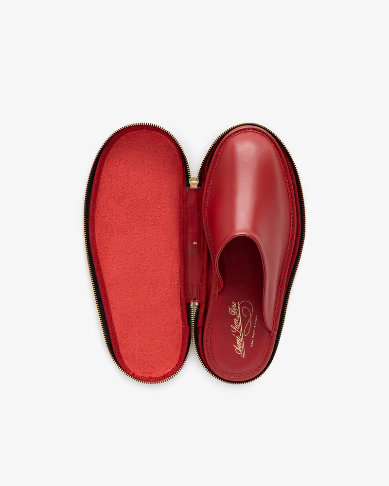 A single Leather Travel Slipper in red, shown inside an open, oval-shaped red zippered case.