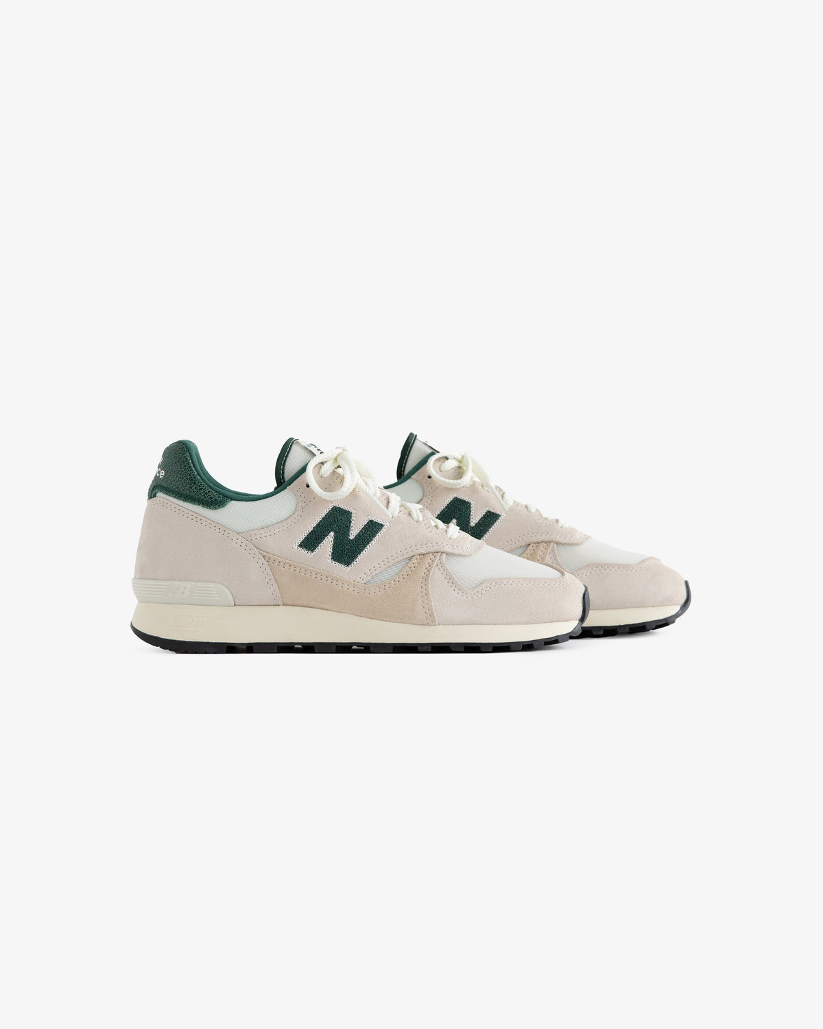 A pair of ALD / New Balance 475 sneakers in beige and green with white laces on a white background.