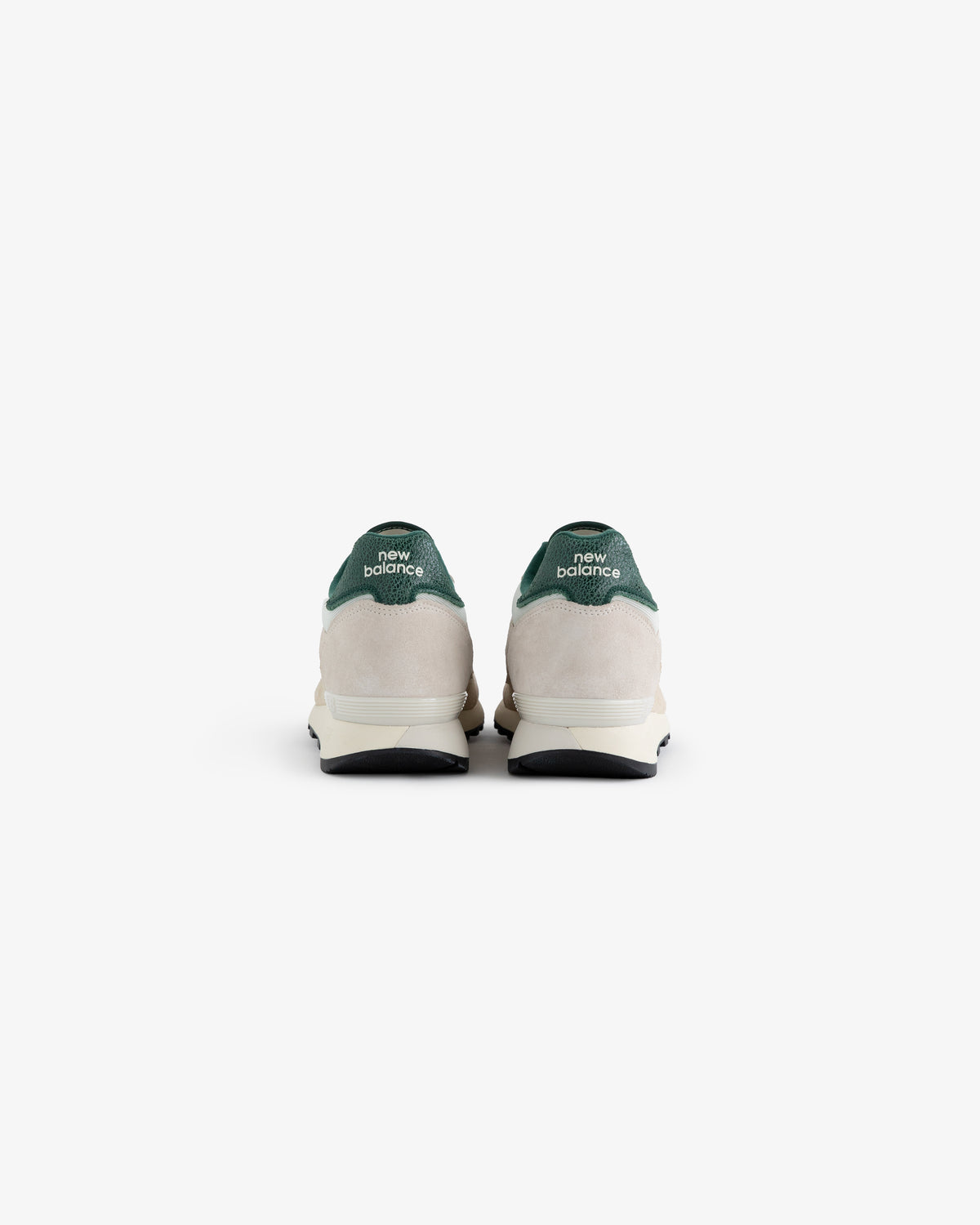 The ALD / New Balance 475 sneakers seen from the back, featuring green heels and white midsoles on a white background.