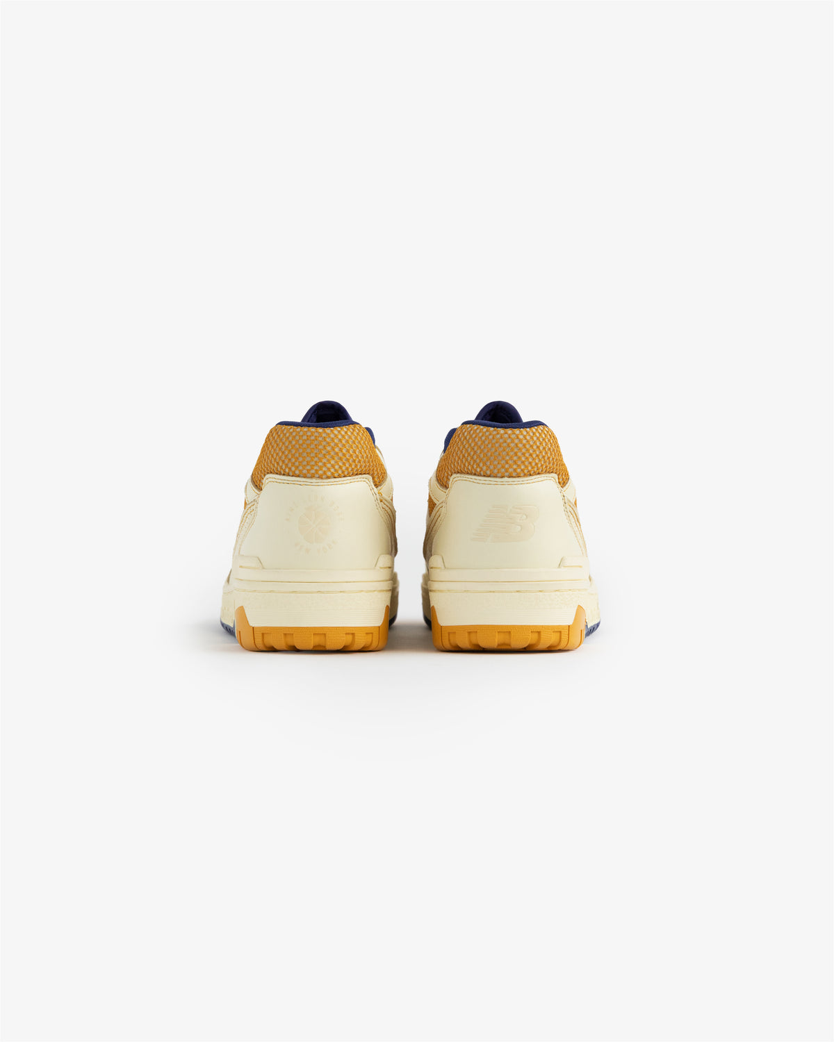 A pair of ALD / NB P550 Basketball Oxfords in cream and yellow viewed from the back against a white background.