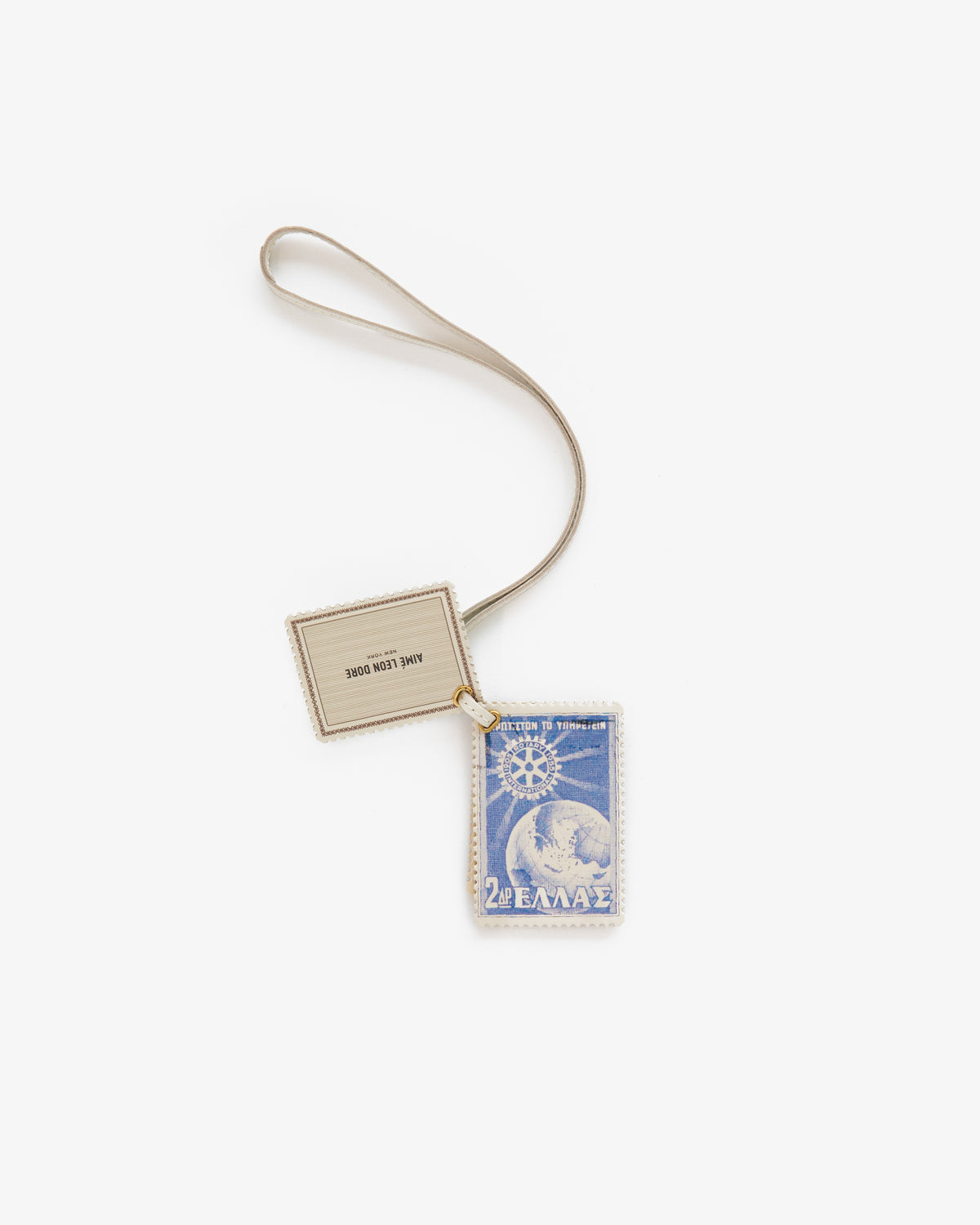 The Leather Traveler Charm features a blue postage stamp with Greek text on a beige tag and strap.