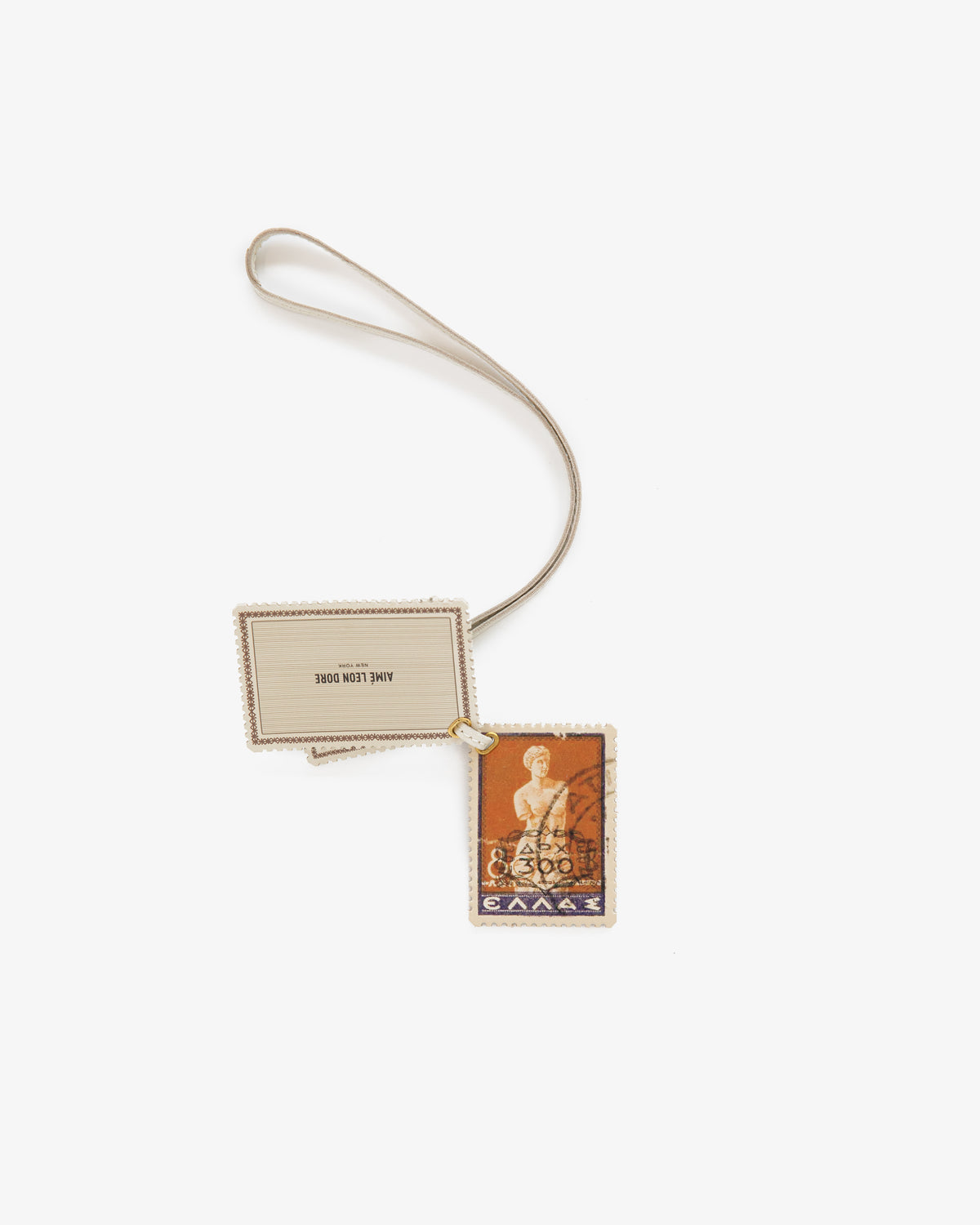 The Leather Traveler Charm is a rectangular keychain with a vintage Greek stamp and beige tag on a looped cord.