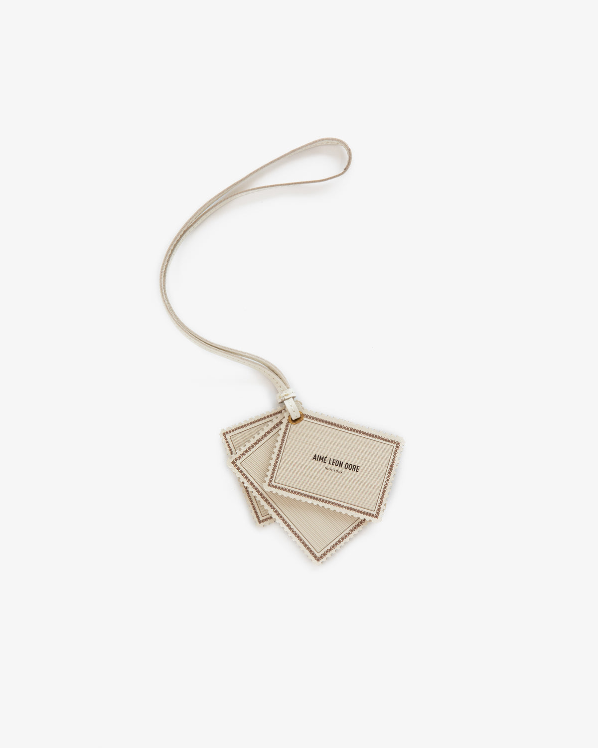 The Leather Traveler Charm is a beige leather luggage tag with AIME LEON DORE text and a matching strap.