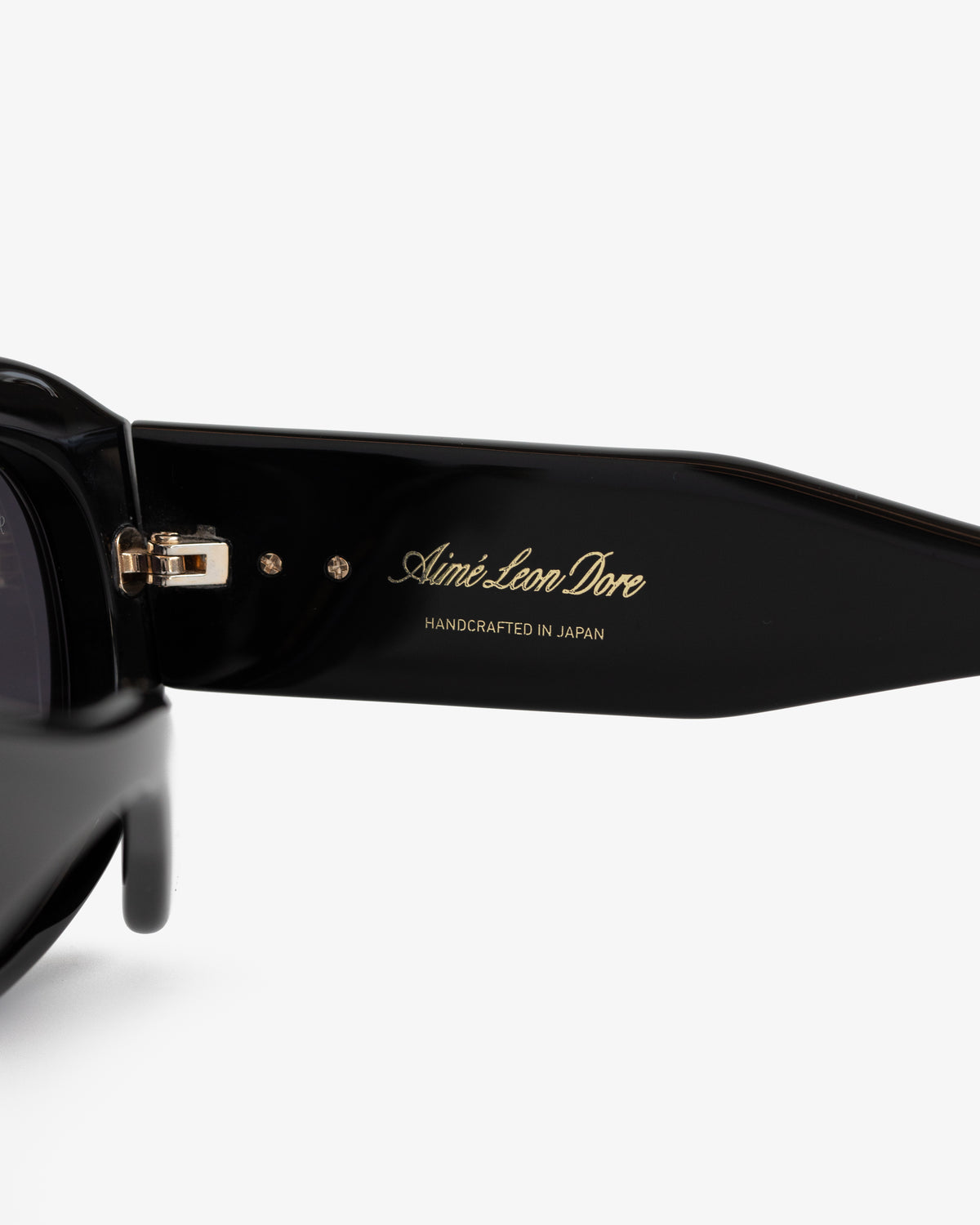Close-up of Jackie O Sunglasses’ black arm with gold Aimé Leon Dore and Handcrafted in Japan engraved text.