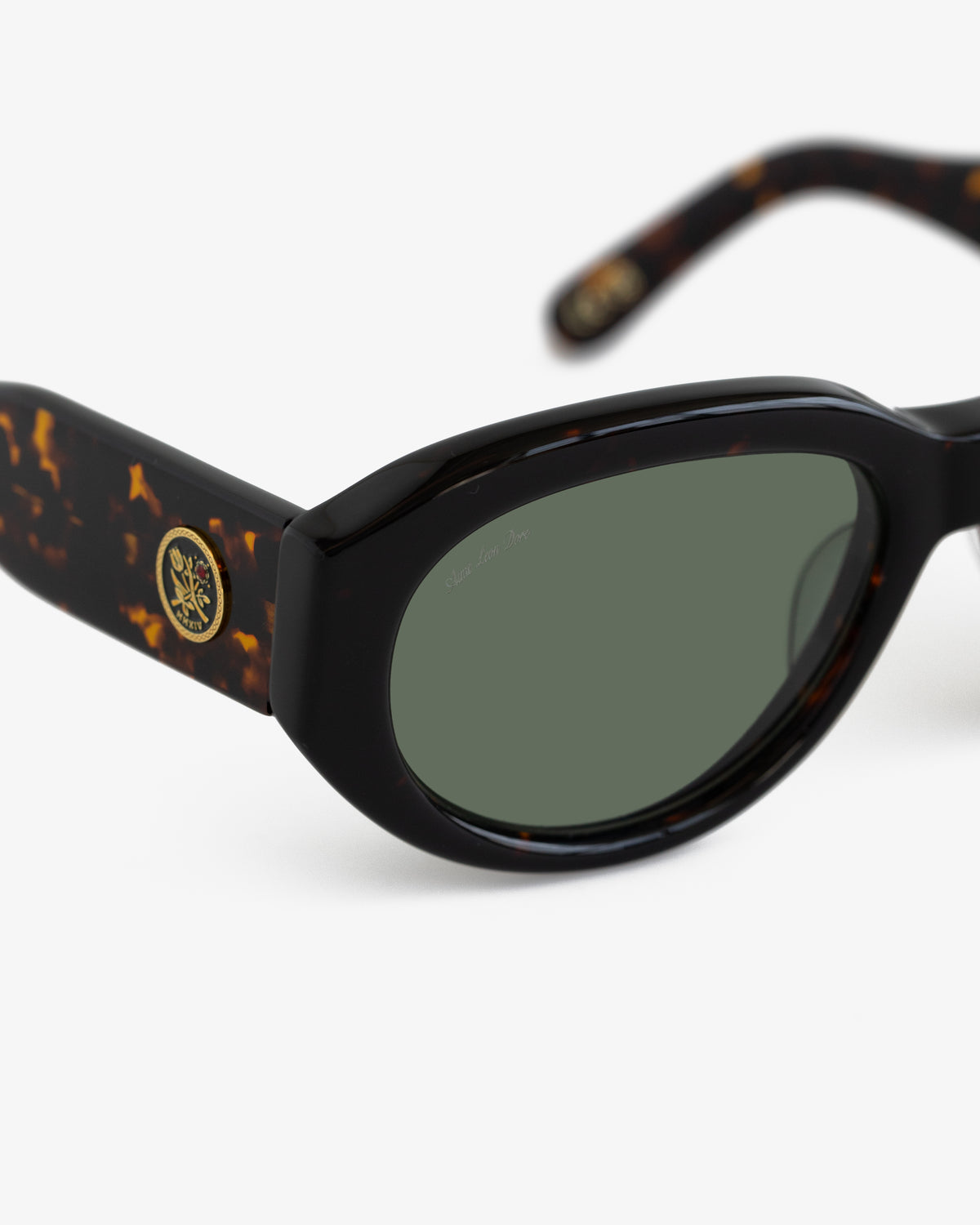Jackie O Sunglasses: Tortoiseshell frame, green lenses, gold temple emblem, displayed on white background.