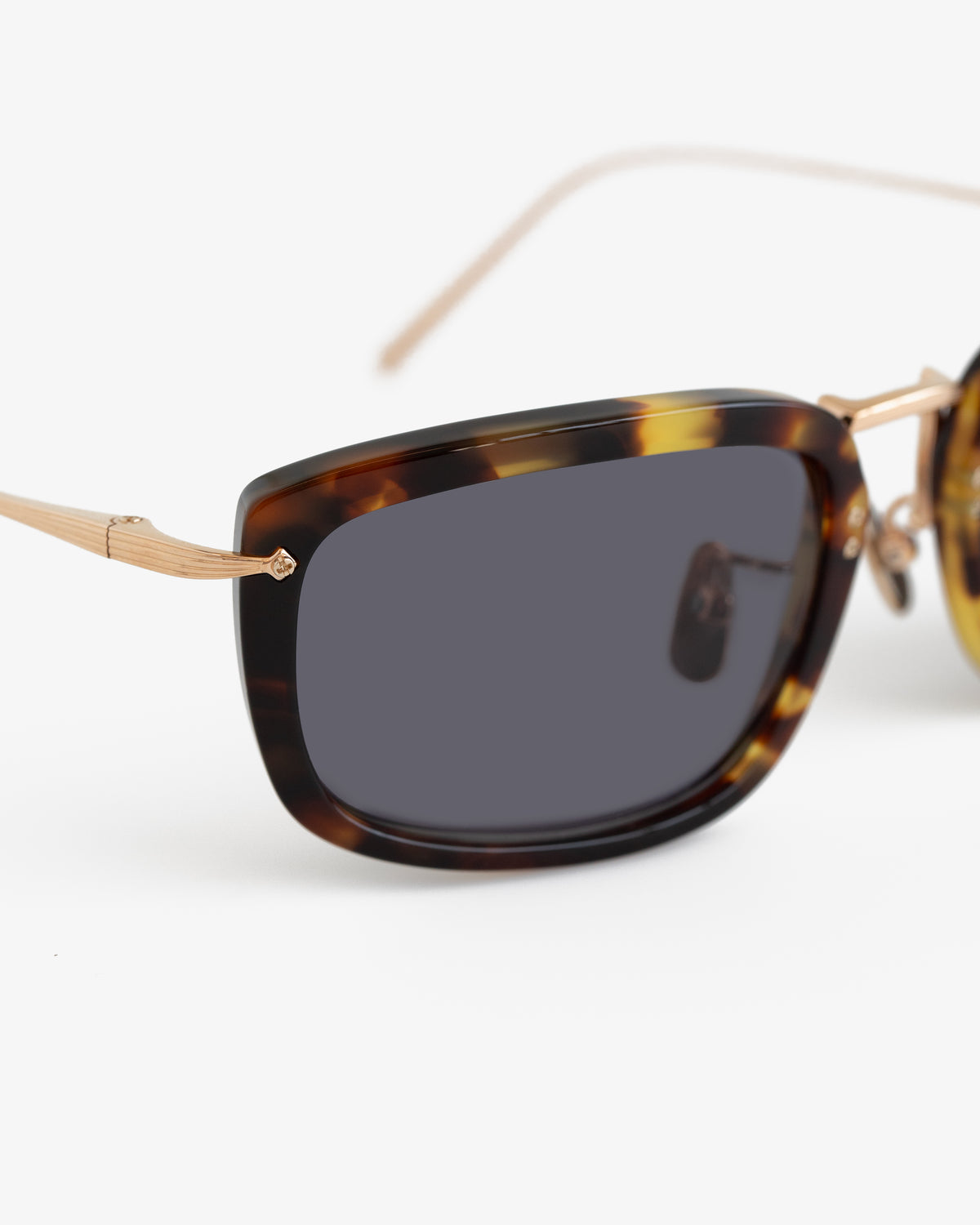 Close-up of Ace Sunglasses featuring tortoiseshell frames, gold arms, and dark lenses against a white background.