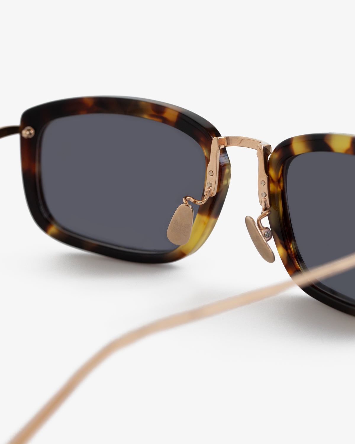 Close-up of Ace Sunglasses—tortoiseshell frame, gold nose bridge, and dark lenses on a white background.