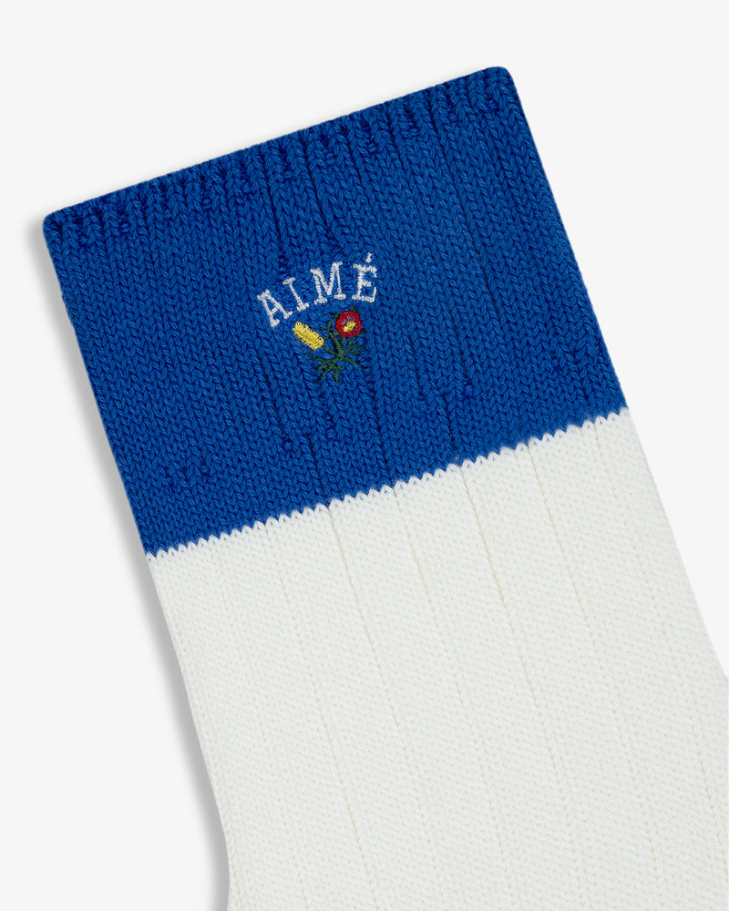 Crest Varsity Sock: White ribbed sock with blue cuff, “AIMÉ” text, and small embroidered flower.