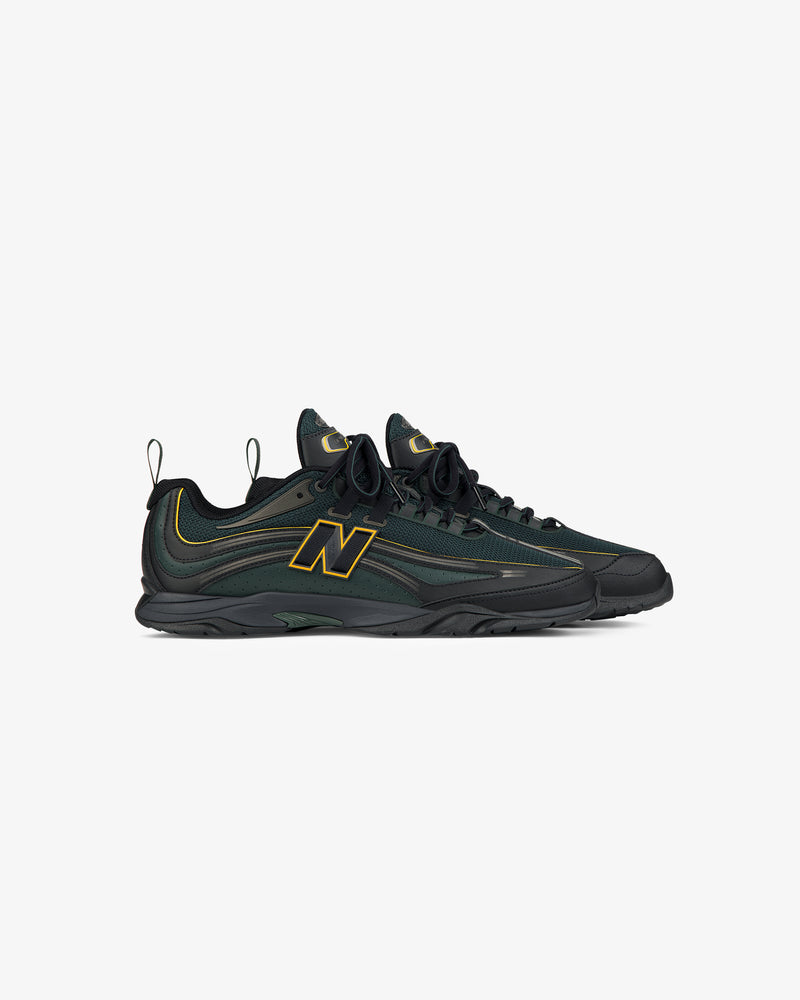 A pair of ALD / New Balance RC56 sneakers in dark green and black with yellow N logos, shown from the side.