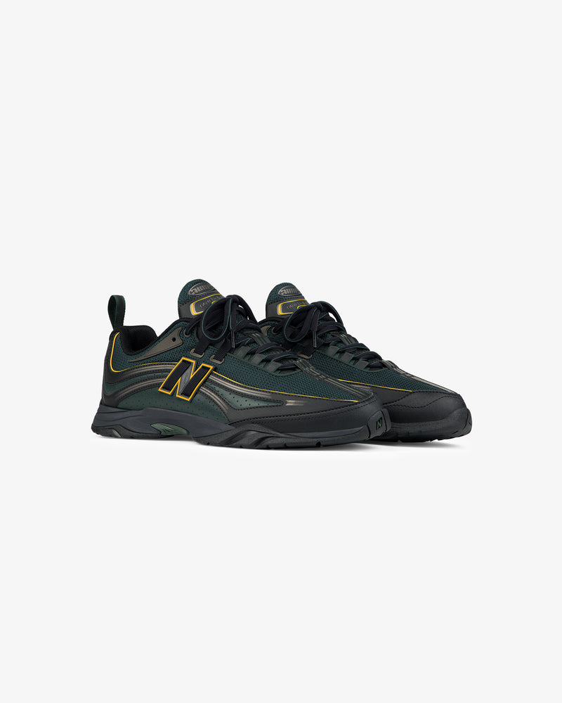 A pair of ALD / New Balance RC56 dark green sneakers with black soles and yellow accents on a white background.