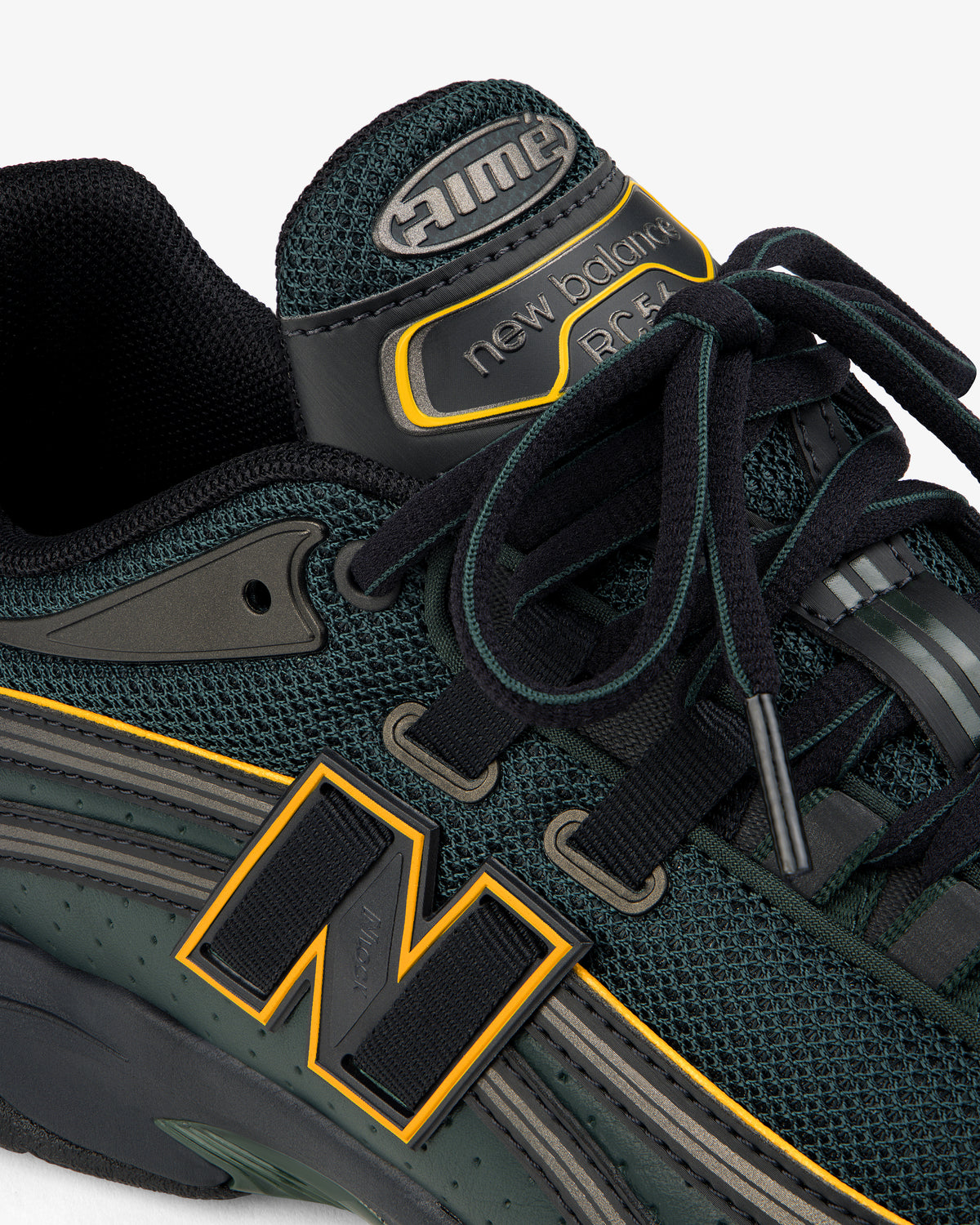 Close-up of a dark green ALD / New Balance RC56 sneaker with yellow accents, black laces, mesh, and leather details.