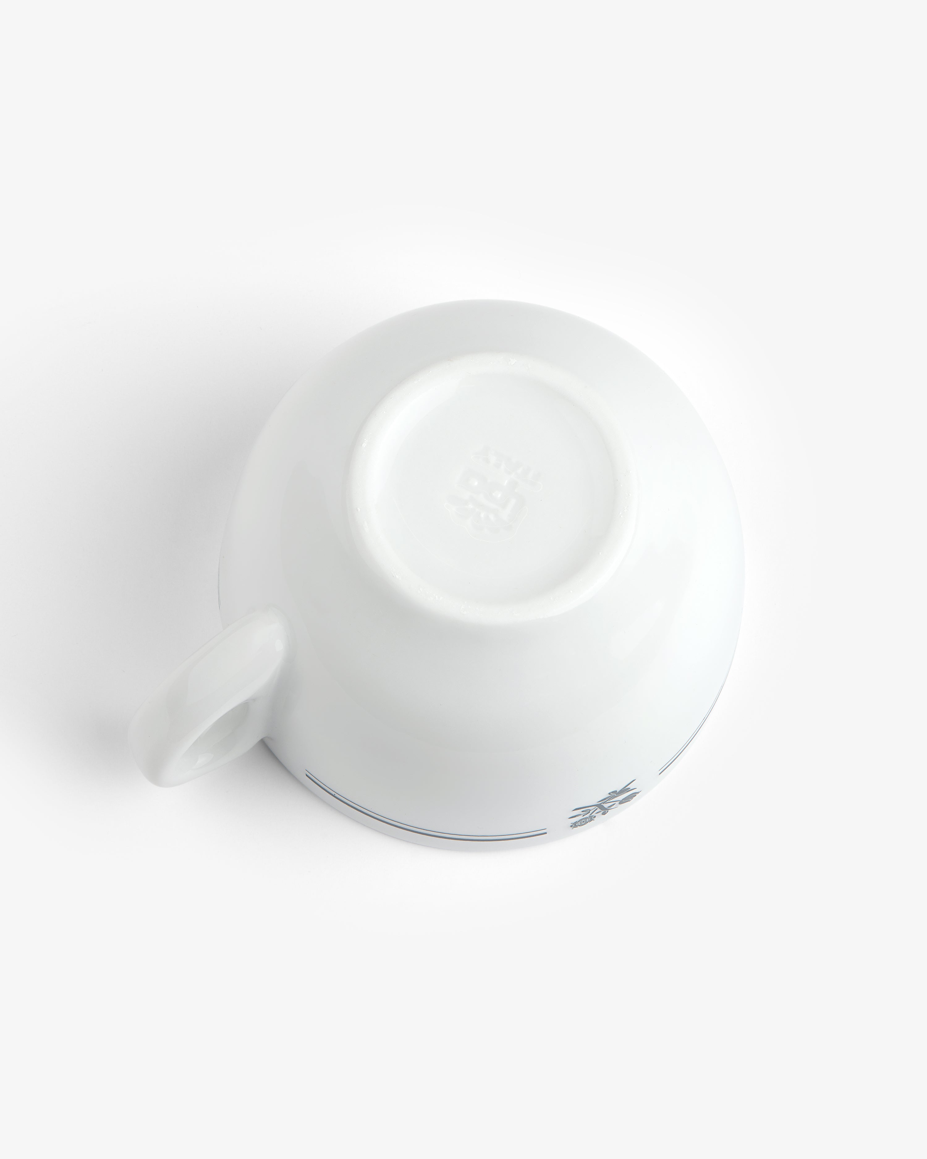 A Café Leon Dore Cappuccino Cup is upside down on a white surface, revealing its base and part of the handle.