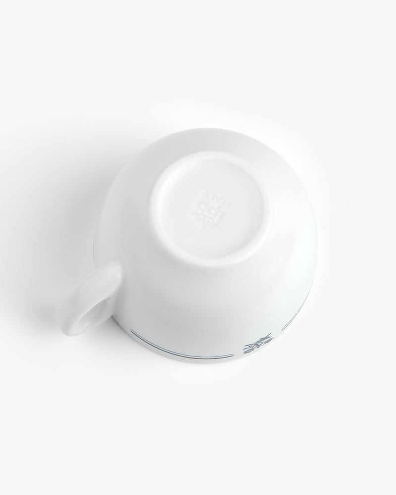 A Café Leon Dore Cappuccino Cup is upside down on a white surface, revealing its base and part of the handle.