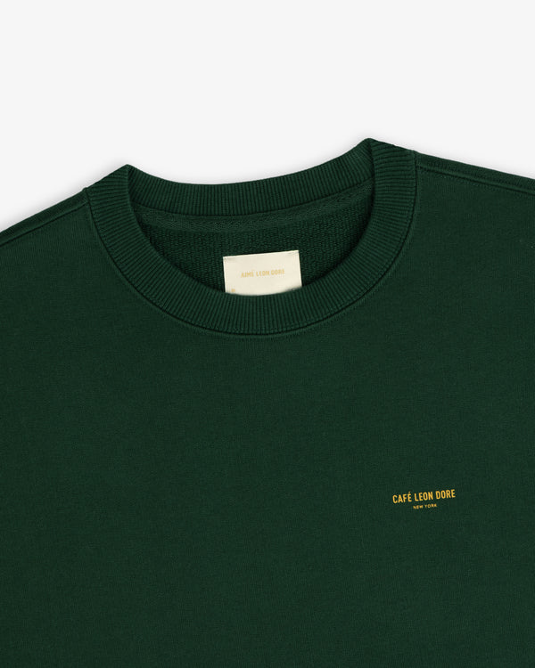 Forest green Café Leon Dore Crewneck with small yellow CAFÉ LEON DORE text on the chest.