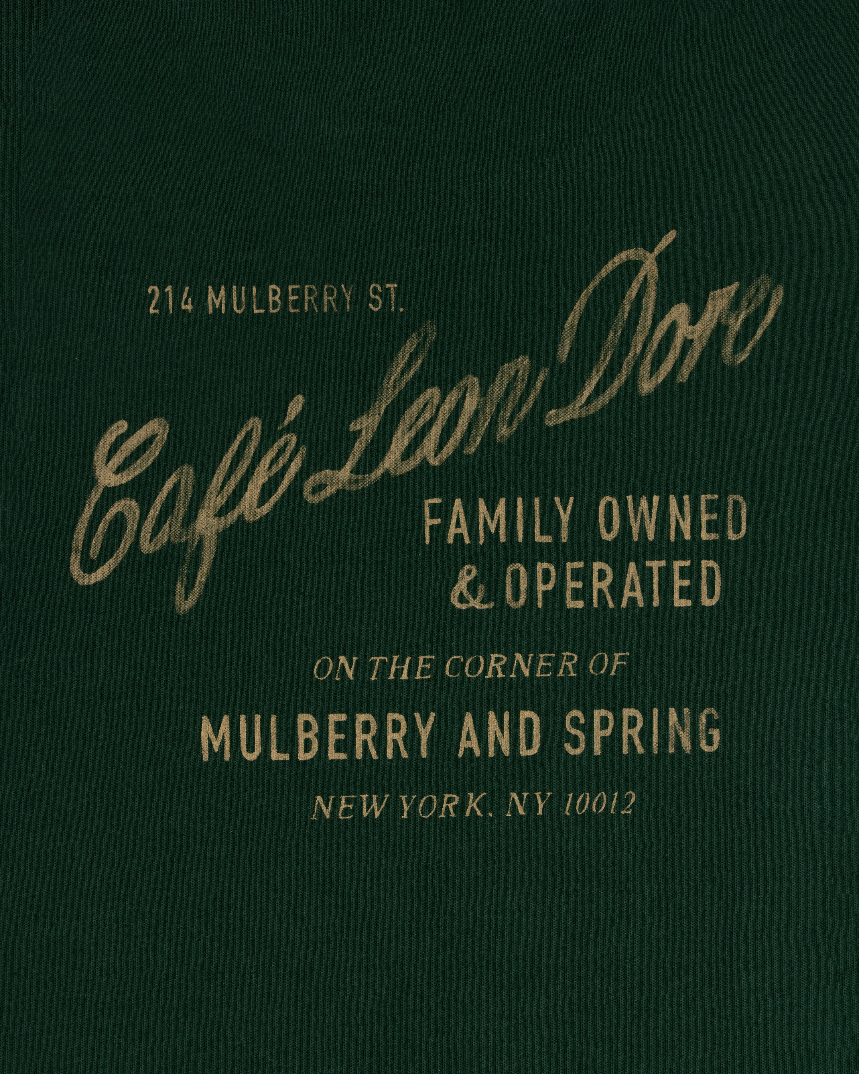 Text on dark green reads: Café Leon Dore Mulberry Tee, family owned, 214 Mulberry St, New York, NY 10012.