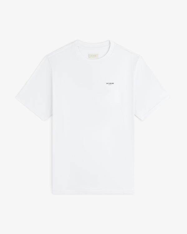 Café Leon Dore Caricature Tee: white short-sleeve shirt with small black text on left chest, on white background.