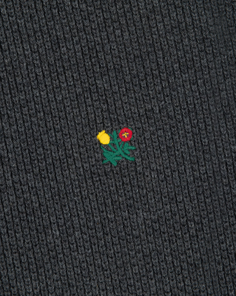 Close-up of Crest Piqué Half-Zip Pullover in black ribbed fabric with a small embroidered yellow-red flower and green leaves.