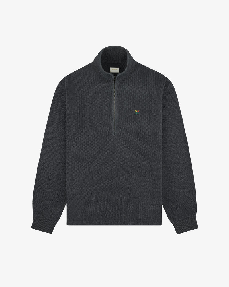 Crest Piqué Half-Zip Pullover in dark gray with a green and yellow logo on the left chest, shown on white background.