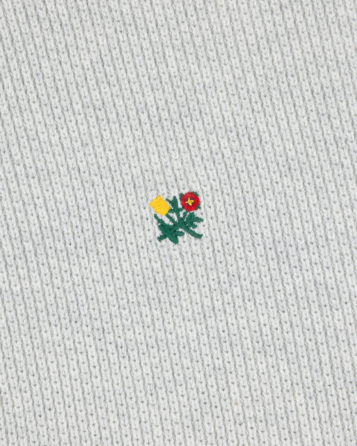 A small yellow and red flower is embroidered on a light gray Crest Piqué Half-Zip Pullover.