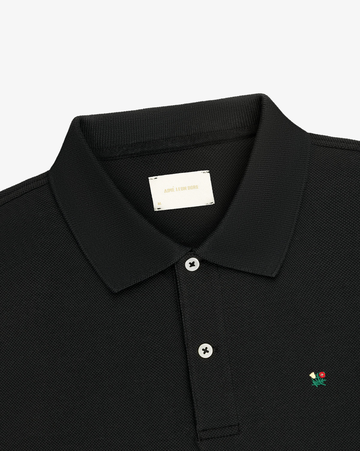 Crest Piqué Polo: Black, collared, two-button shirt with small embroidered flower on the chest.