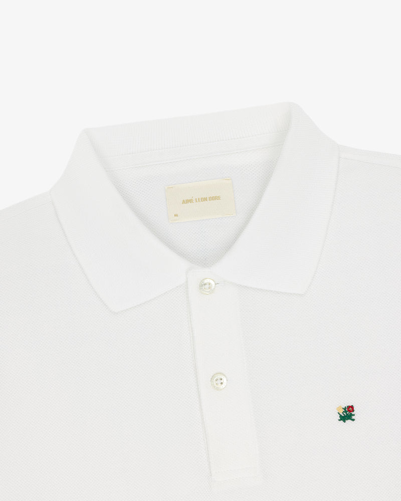 Crest Piqué Polo: white, collared, three-button shirt with a small green and red chest logo.