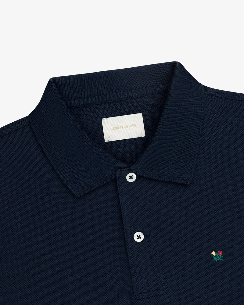 Crest Piqué Polo in navy with small floral chest embroidery and white buttons, laid flat on a white background.