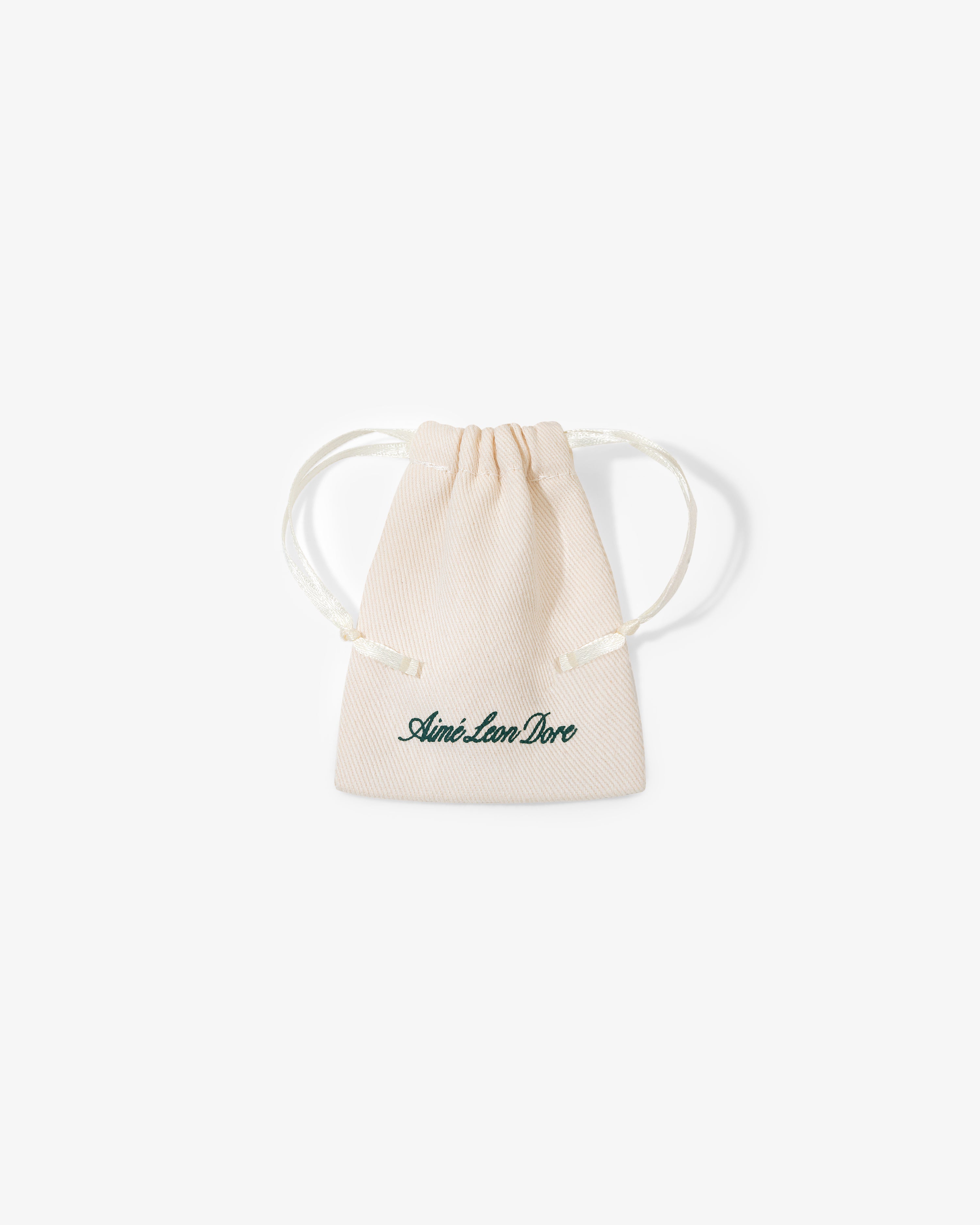 A small beige drawstring pouch with "Queens Crest Penny" printed in green script on the front.