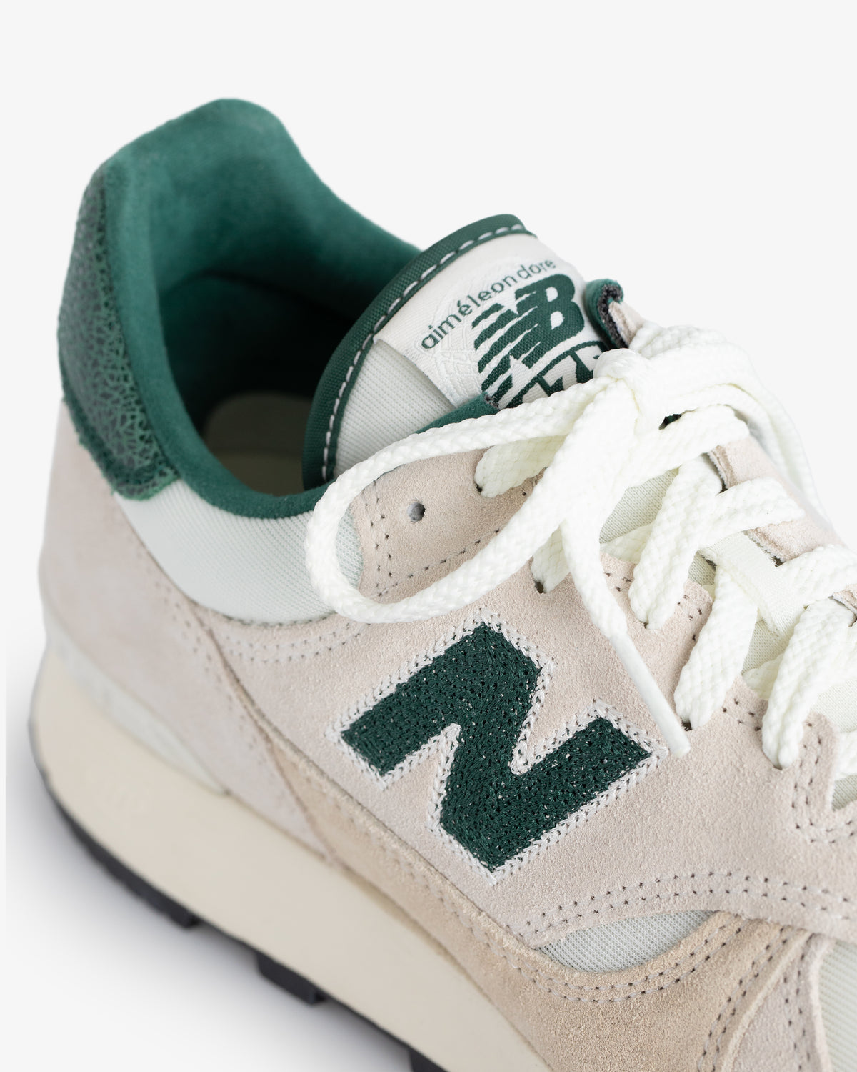 Close-up of an ALD / New Balance 475 sneaker in beige and green with white laces and a suede finish.