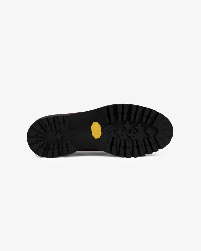 The image shows the black rubber sole of the Suede Derby Hiker with a yellow logo in the center, viewed from below.