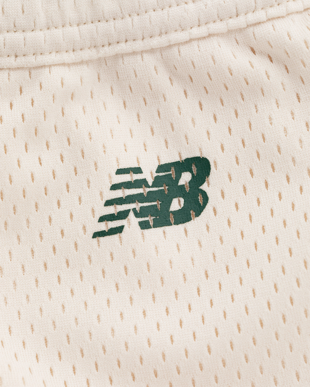Close-up of a green New Balance logo on beige perforated ALD / New Balance SONNY NY Gym Short fabric.