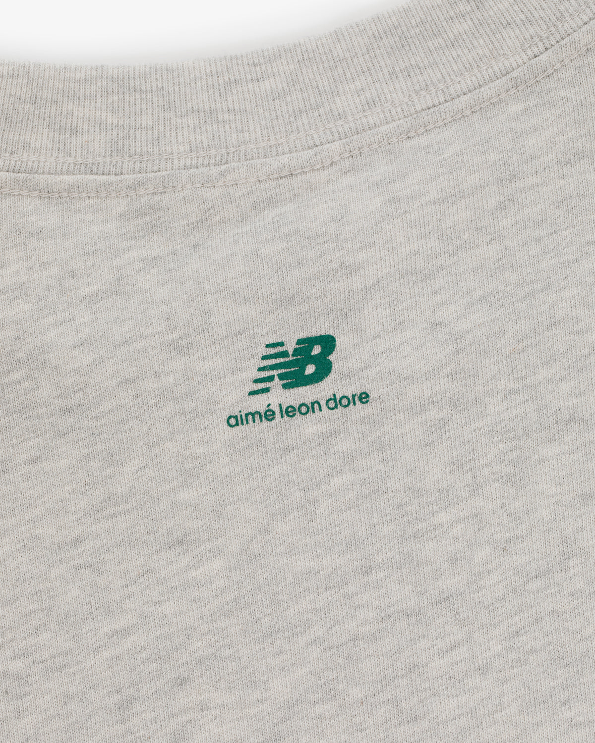 Close-up of the ALD / New Balance SONNY NY Long-Sleeve Tee with green logos on light gray fabric.