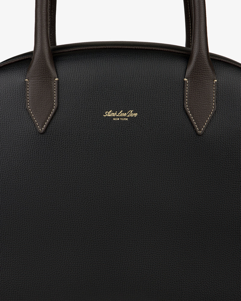 Close-up of the Full Grain Leather Crescent Shoulder Bag in black with brown handles and gold Sloan Ian Dove New York text.