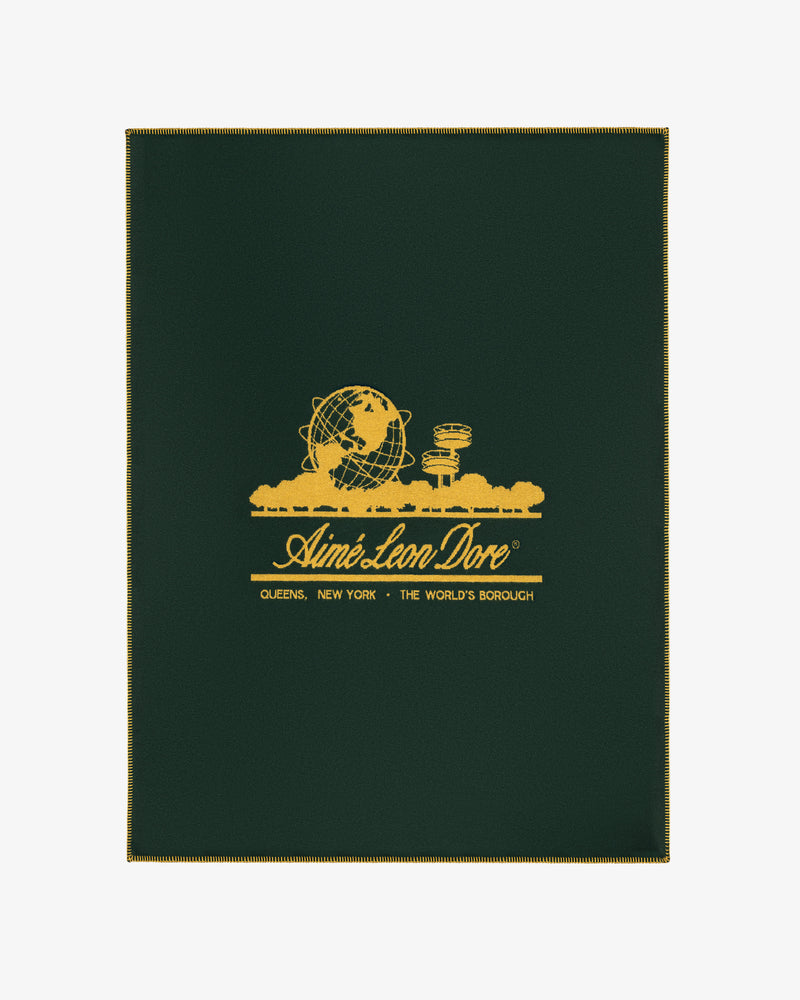 Dark green Unisphere Wool Blanket with gold globe and cityscape graphic, and Aimé Leon Dore text with location details.