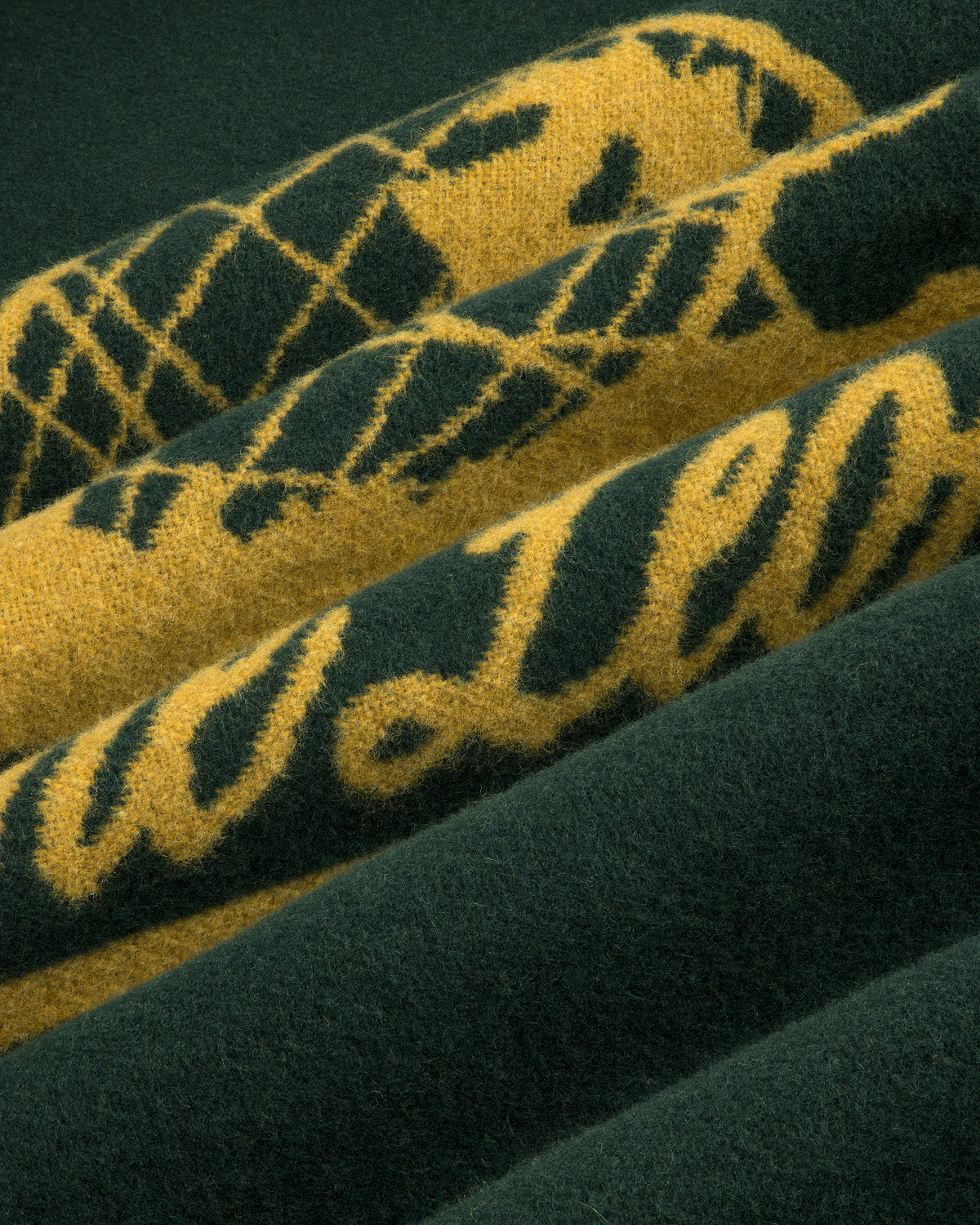 Close-up of textured green and yellow Unisphere Wool Blanket with pattern and partial script on folded layers.