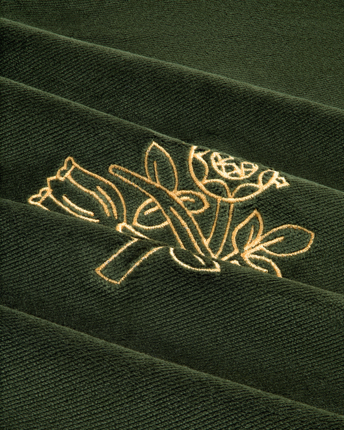 Queens Crest Throw Pillow: Gold embroidered rose and tulip design on dark green, ribbed fabric with diagonal folds.