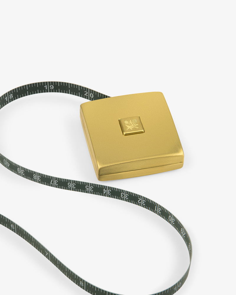 The Queens Crest Brass Tape Measure features a gold square case and black tape, displayed on a white background.