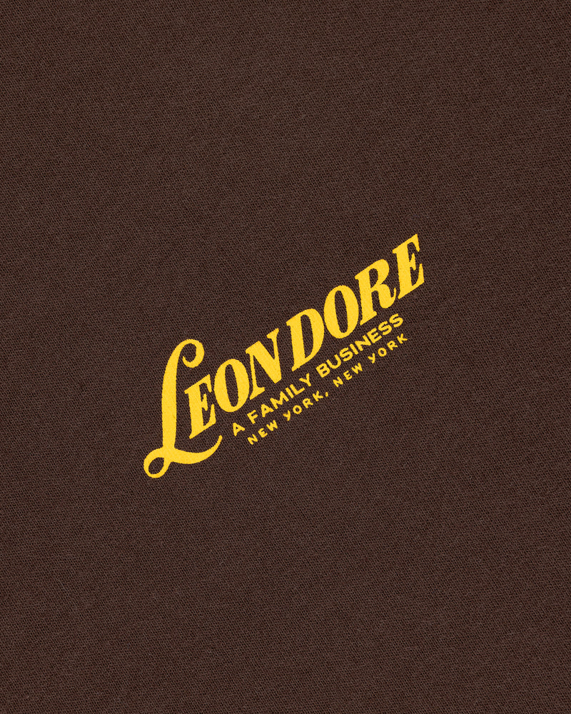Brown Leon Dore Tee with yellow text: “LEON DORE – A FAMILY BUSINESS – NEW YORK, NEW YORK.”.