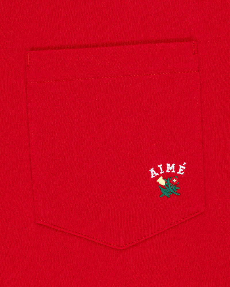 Crest Pocket Tee with AIMÉ text over an embroidered green leaf and cream flower on the red shirt pocket.