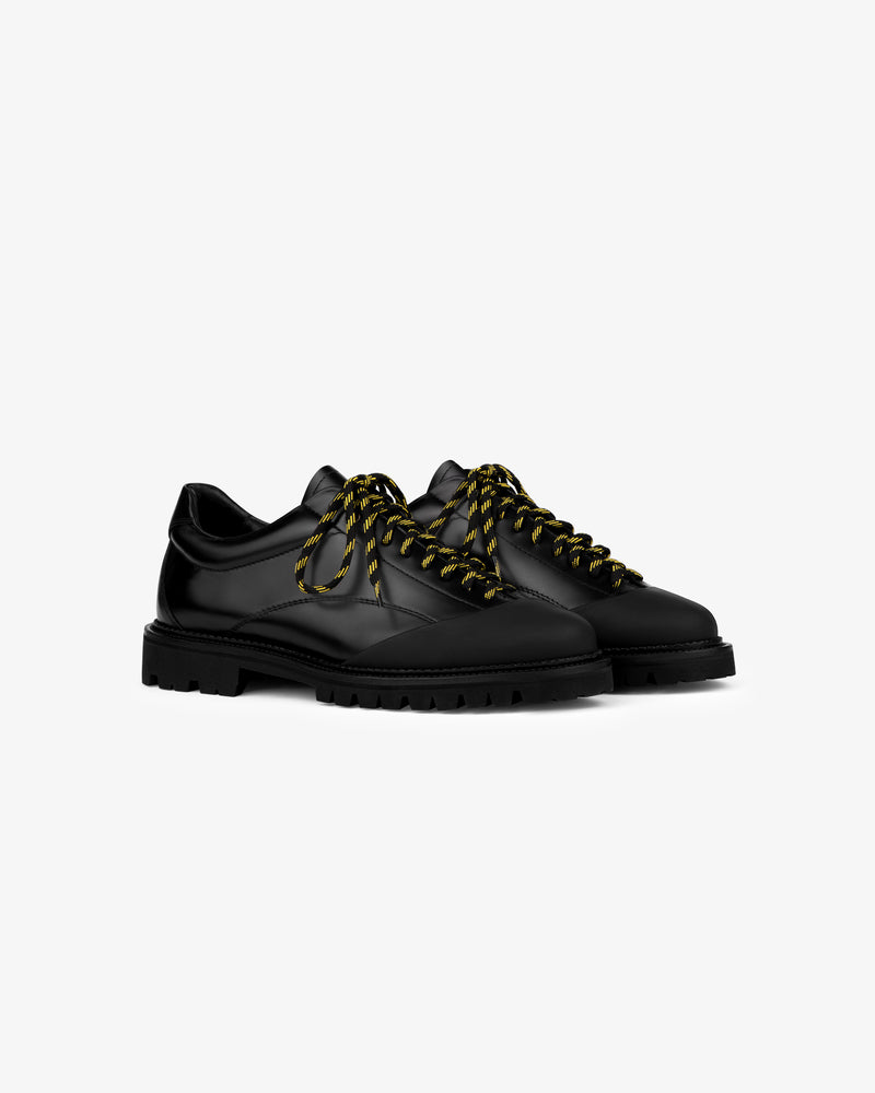 The Leather Derby Hiker: black leather lace-up shoes with thick soles and striped laces on a white background.