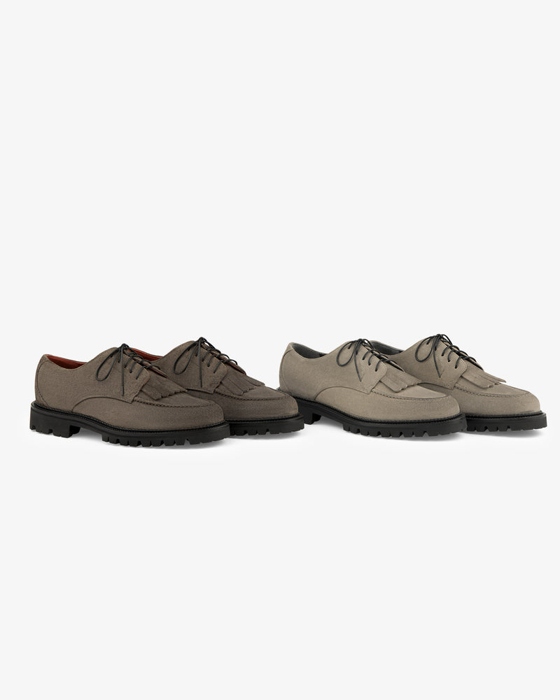 Two pairs of Suede Lug Sole Derby shoes in taupe and beige with black lug soles, on a white background.