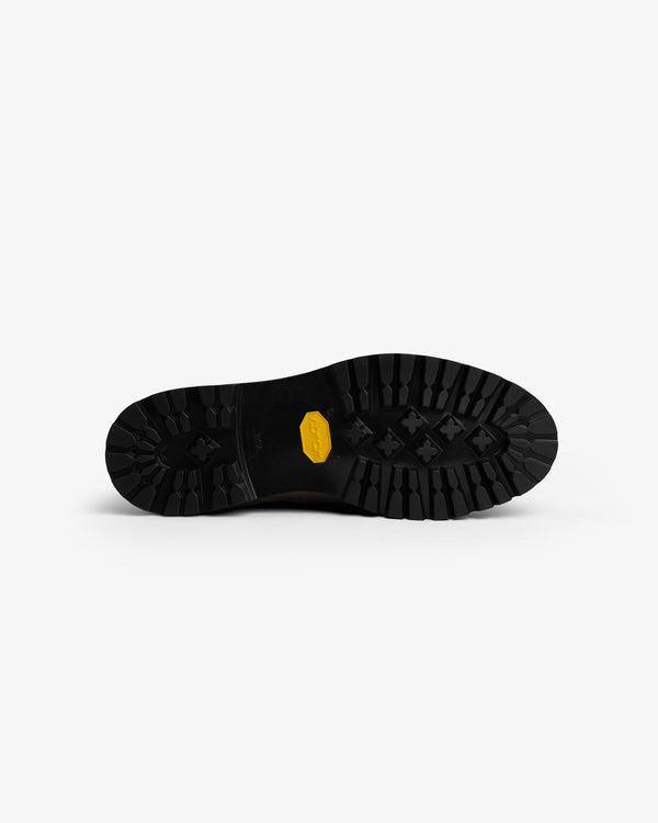 Black lugged rubber sole of a Suede Lug Sole Derby with a yellow logo embedded in the center.