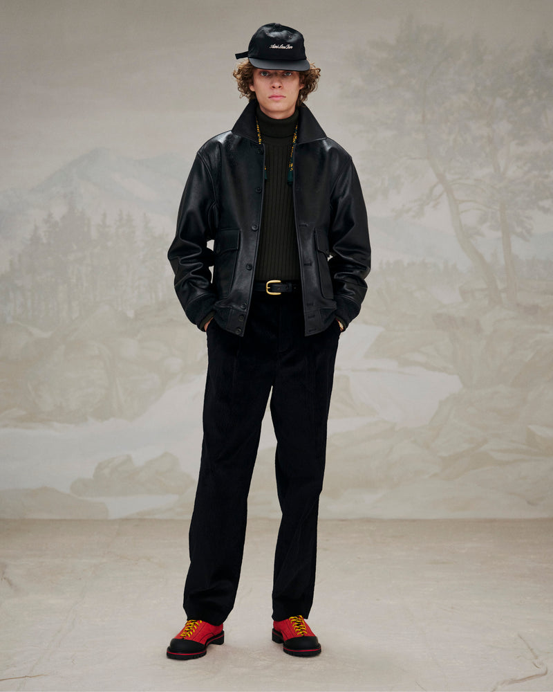 Person wearing Suede Derby Hiker, black leather jacket, black pants, and black cap indoors against a nature backdrop.