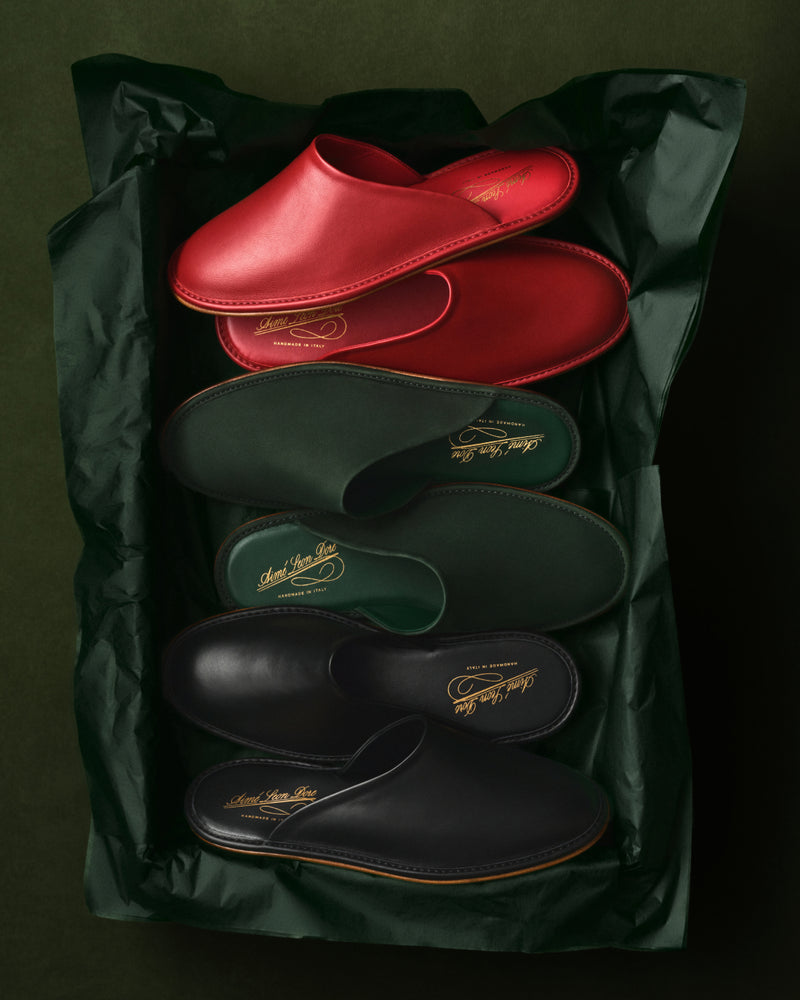 Three pairs of Leather Travel Slippers in red, green, and black on green tissue paper in a box.