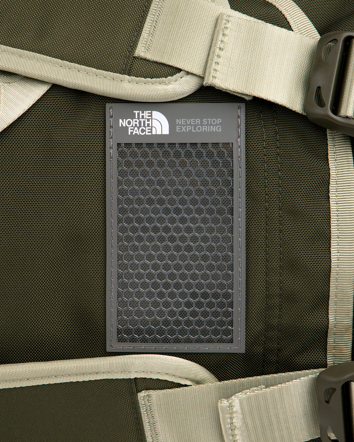 Close-up of ALD / The North Face Base Camp Duffel logo patch on a dark green backpack with beige straps and buckles.