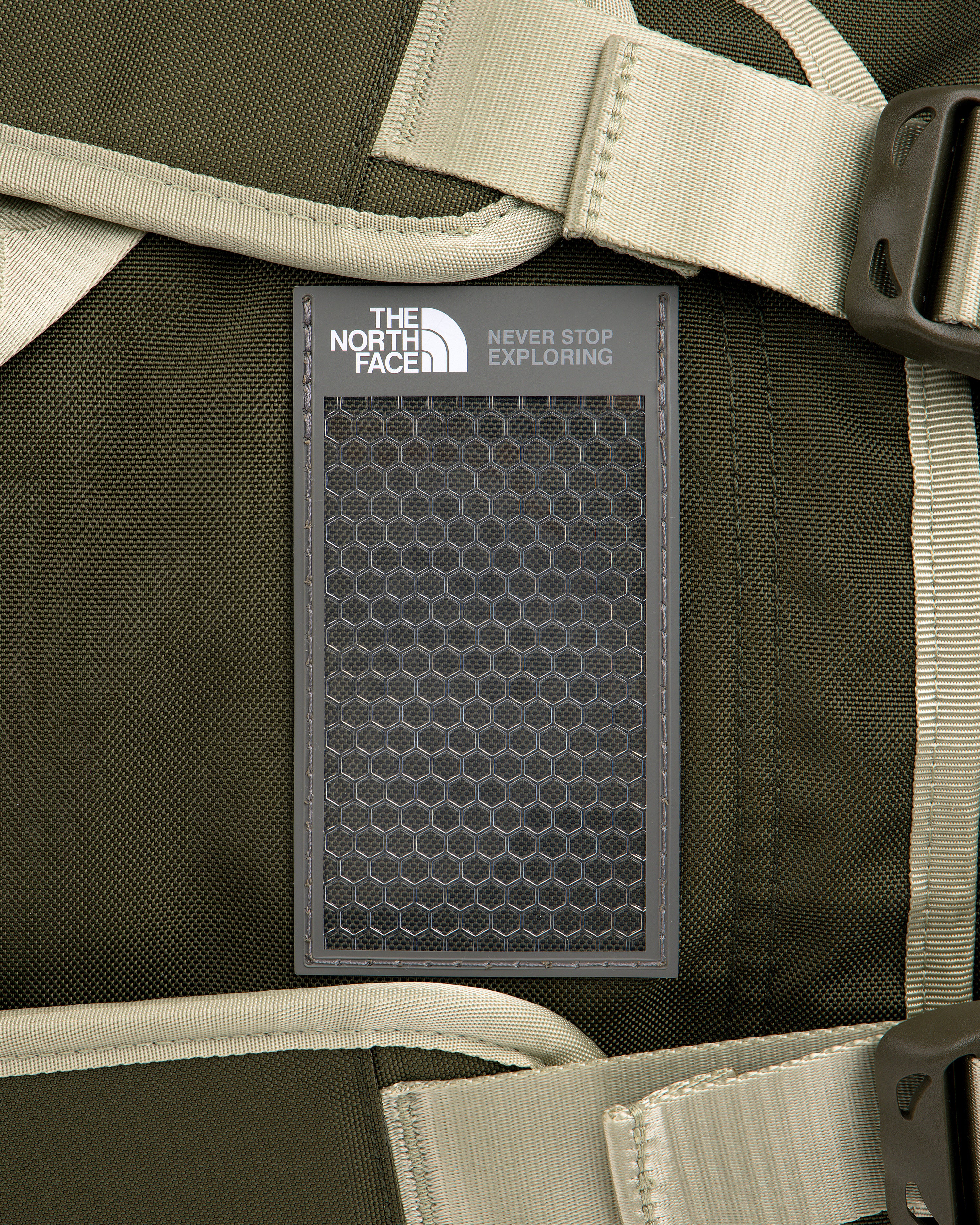 Close-up of ALD / The North Face Base Camp Duffel logo patch on a dark green backpack with beige straps and buckles.