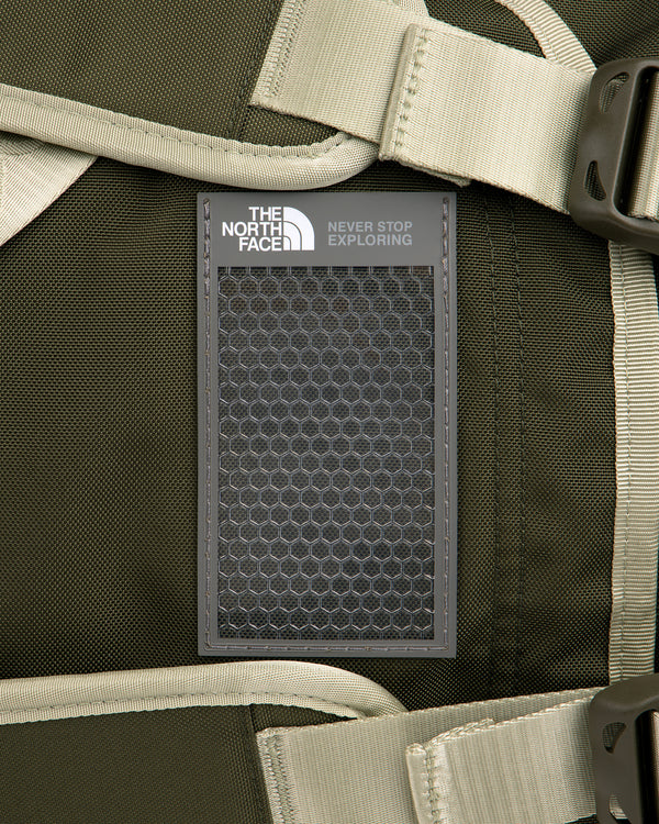 Close-up of ALD / The North Face Base Camp Duffel logo patch on a dark green backpack with beige straps and buckles.