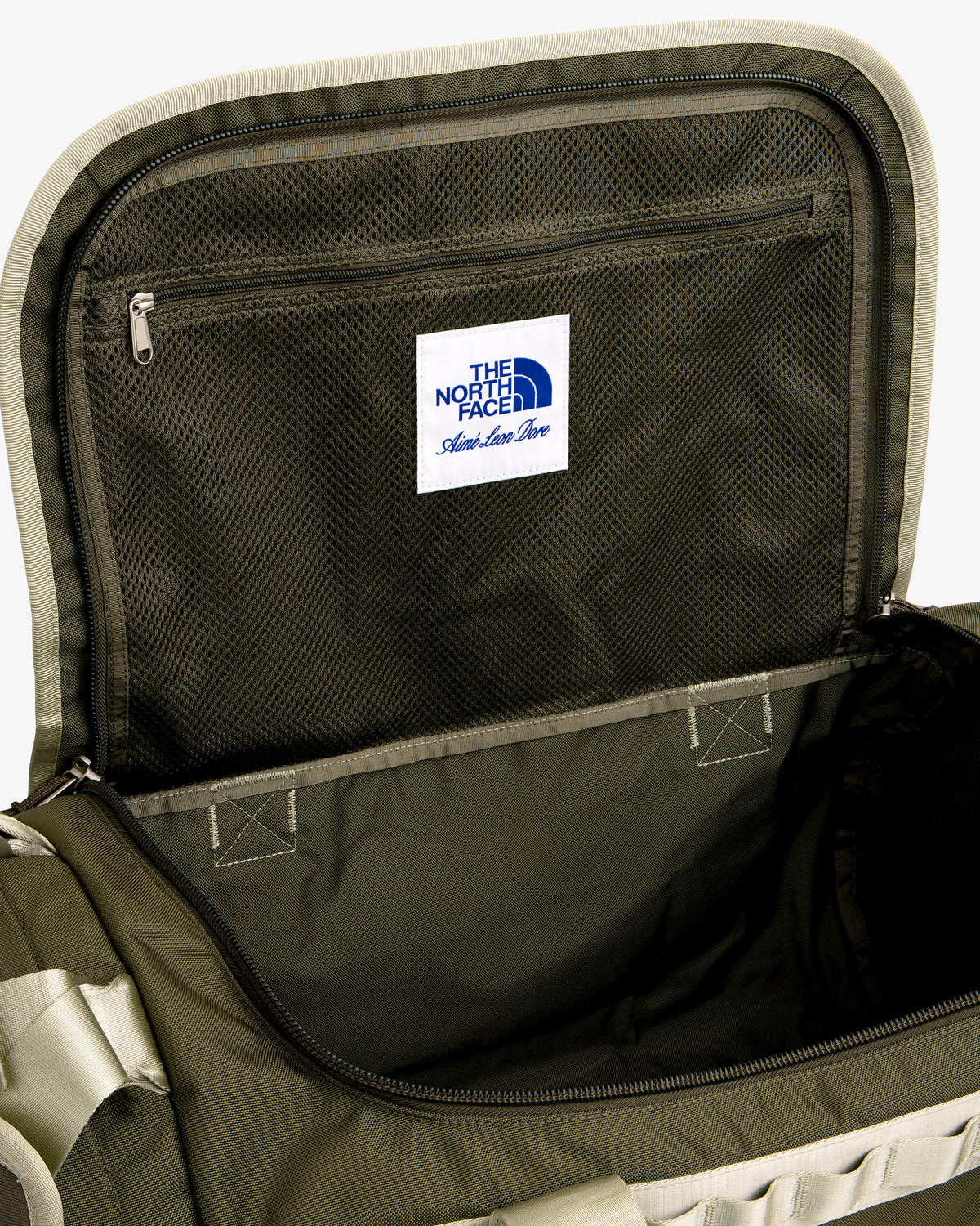 Open olive green ALD / The North Face Base Camp Duffel showing mesh pocket, zipper, and label inside the lid.