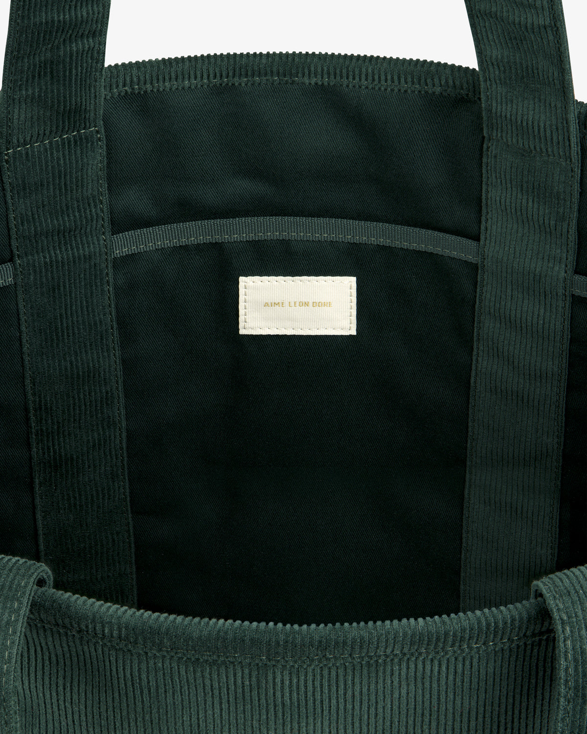 Interior of a dark green Large Corduroy Unisphere Tote Bag with a centered off-white fabric label.